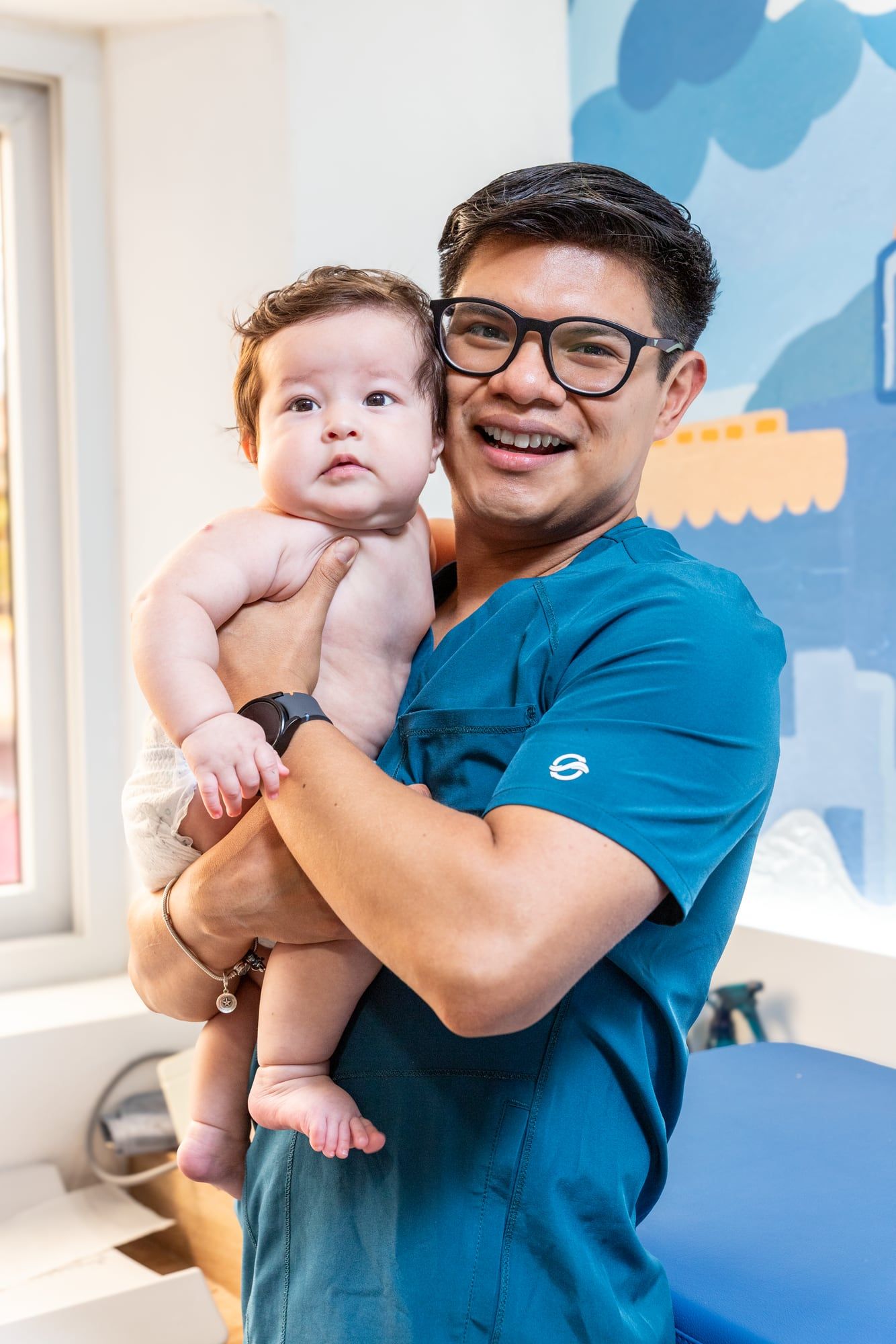 Pediatra sonriendo con un bebé en brazos en su consultorio